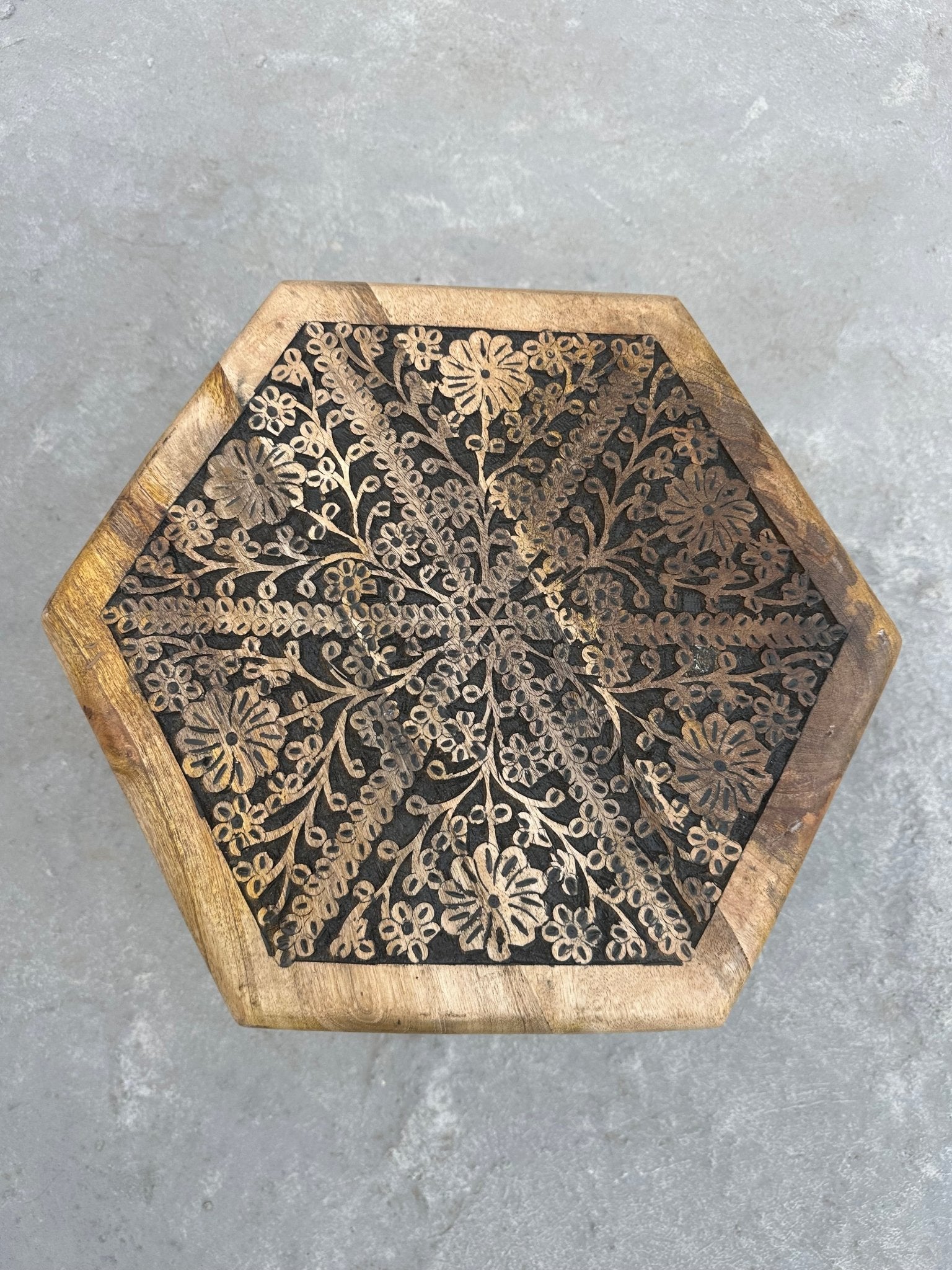 Hexagonal wooden coaster with floral patterns on a gray surface