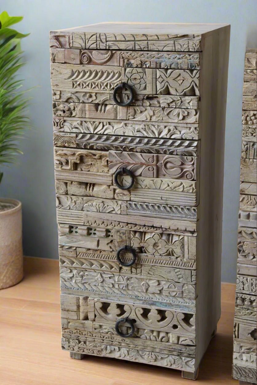 Wooden dresser with intricate carvings against a white brick wall.