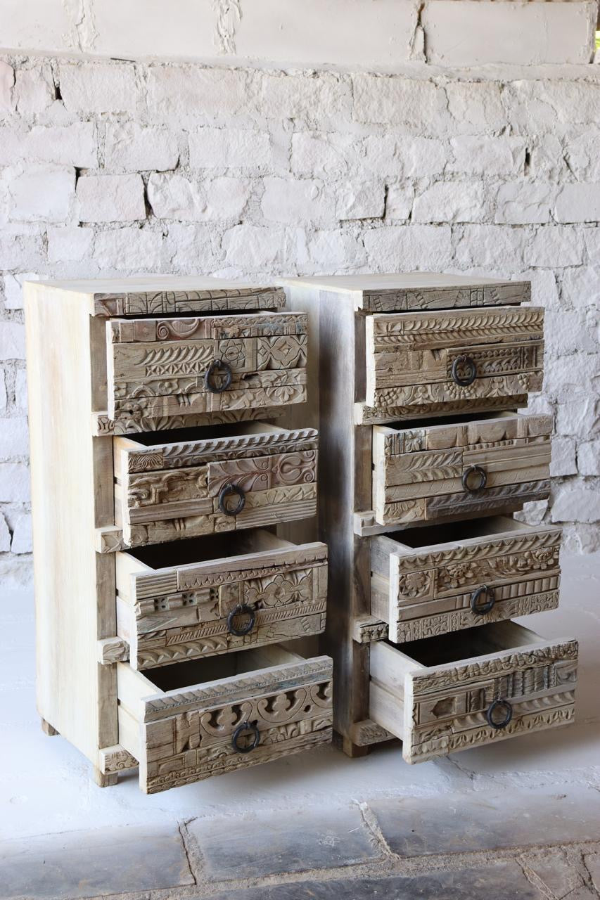A rustic wooden chest with four drawers featuring hand-carved details and antique iron ring pulls, placed in a living room setting. 
