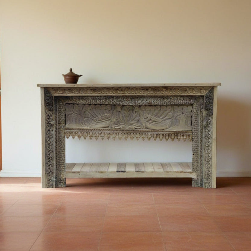 Decorative wooden console table with intricate carvings in a room with tiled floor and white walls.