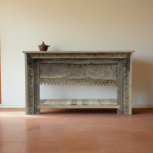 Decorative wooden console table with intricate carvings in a room with tiled floor and white walls.