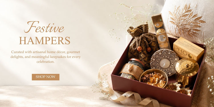 A festive gift hamper box filled with decorative home decor items, including a small fabric bag, candle, ornaments, and wooden keepsakes, shown on a warm cream background 