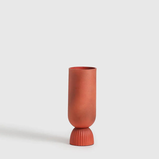 Made from durable aluminium and finished with a smooth powder-coated polish, this vase features a striking silhouette: a sleek cylindrical body perched gracefully on a ribbed, pod-shaped pedestal.