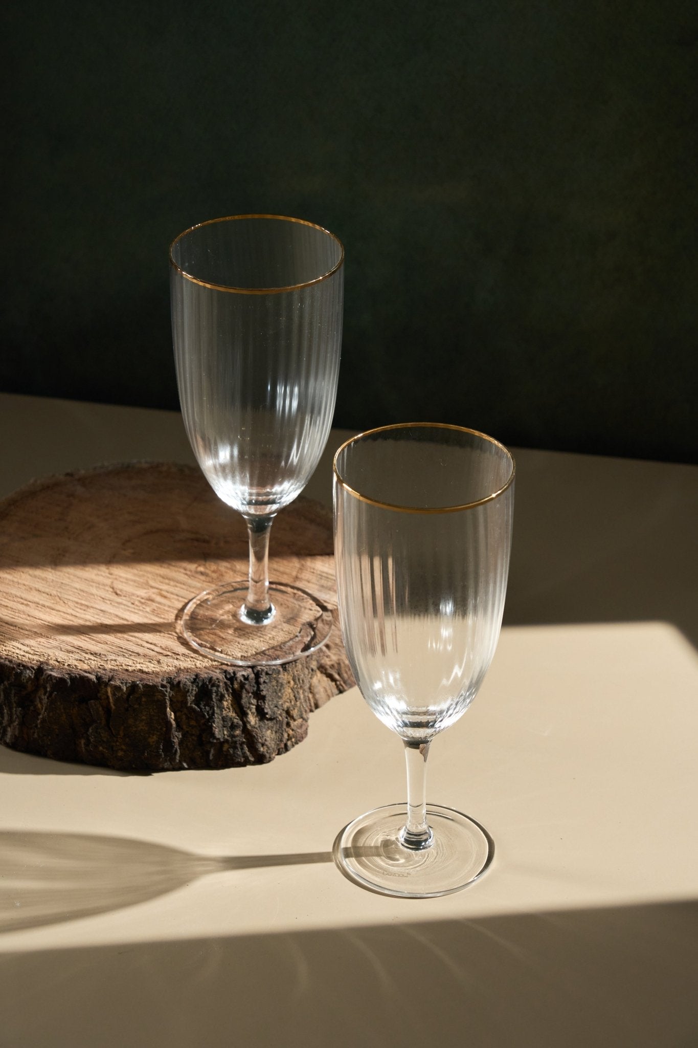 Two clear wine glasses with gold rims on a wooden surface against a dark background