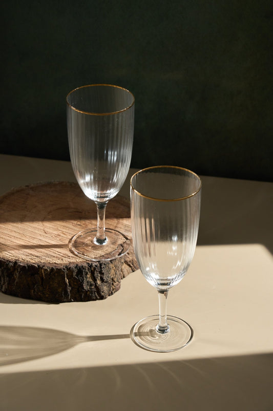 Two clear wine glasses with gold rims on a wooden surface against a dark background