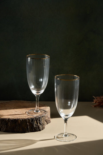 Two clear wine glasses with gold rims on a wooden surface against a dark background