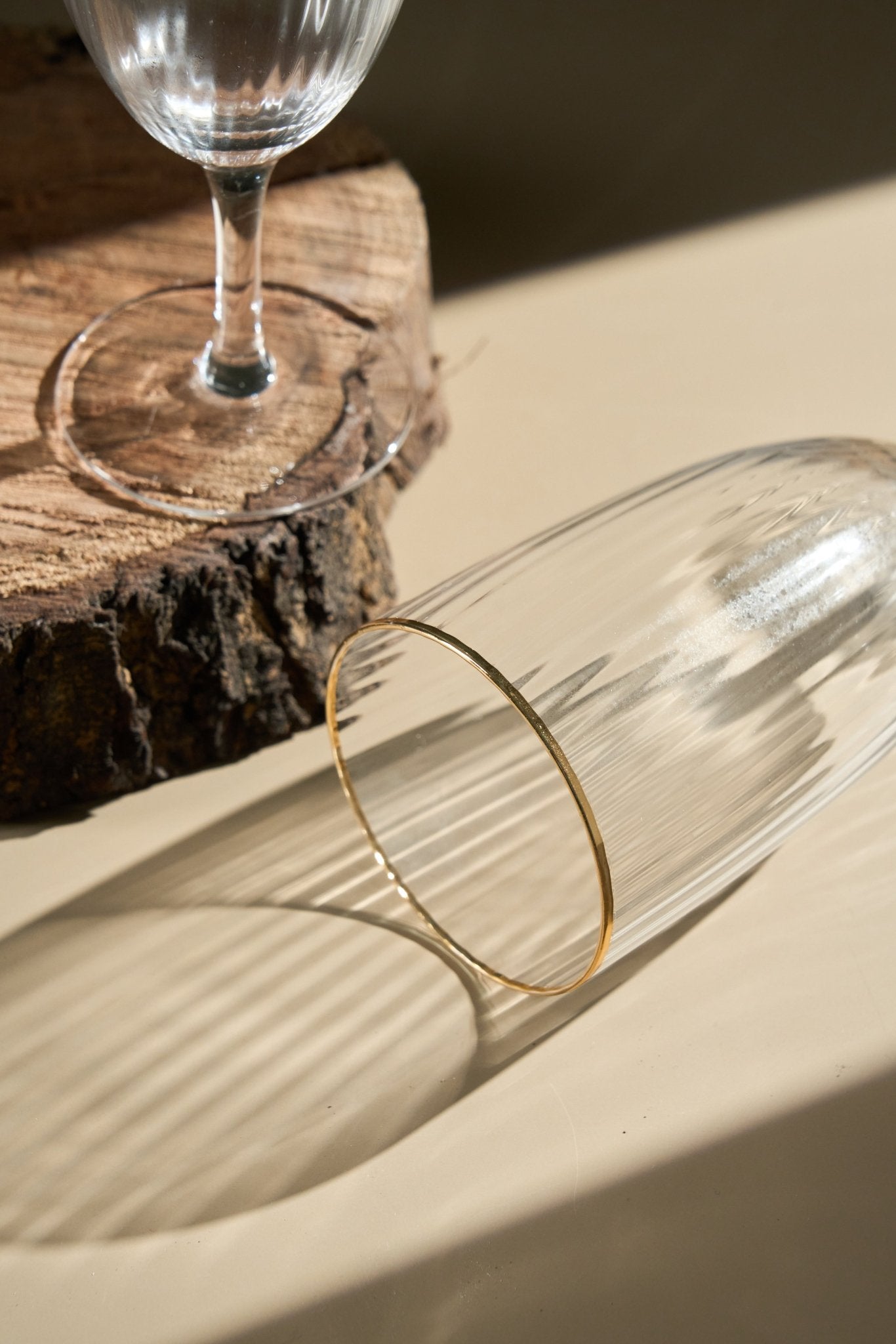 Gold bracelet on a glass surface with a wine glass in the background