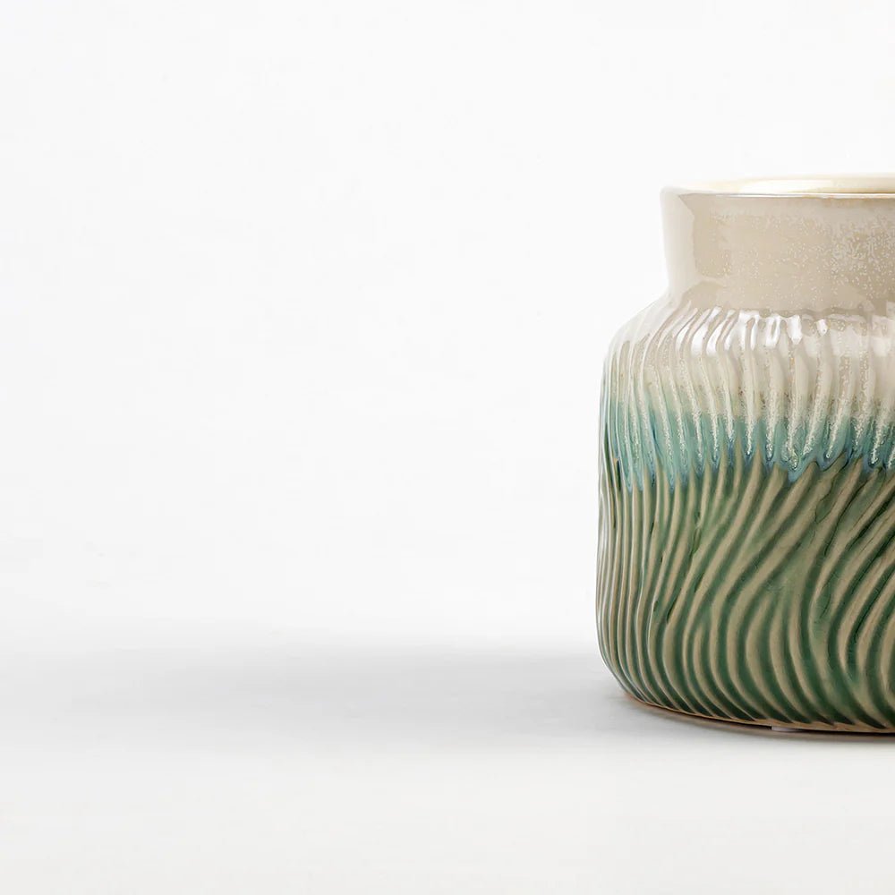 Ceramic vase with wavy green and white design on a white background
