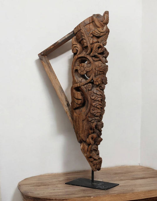 Carved wooden bracket on a stand against a white wall