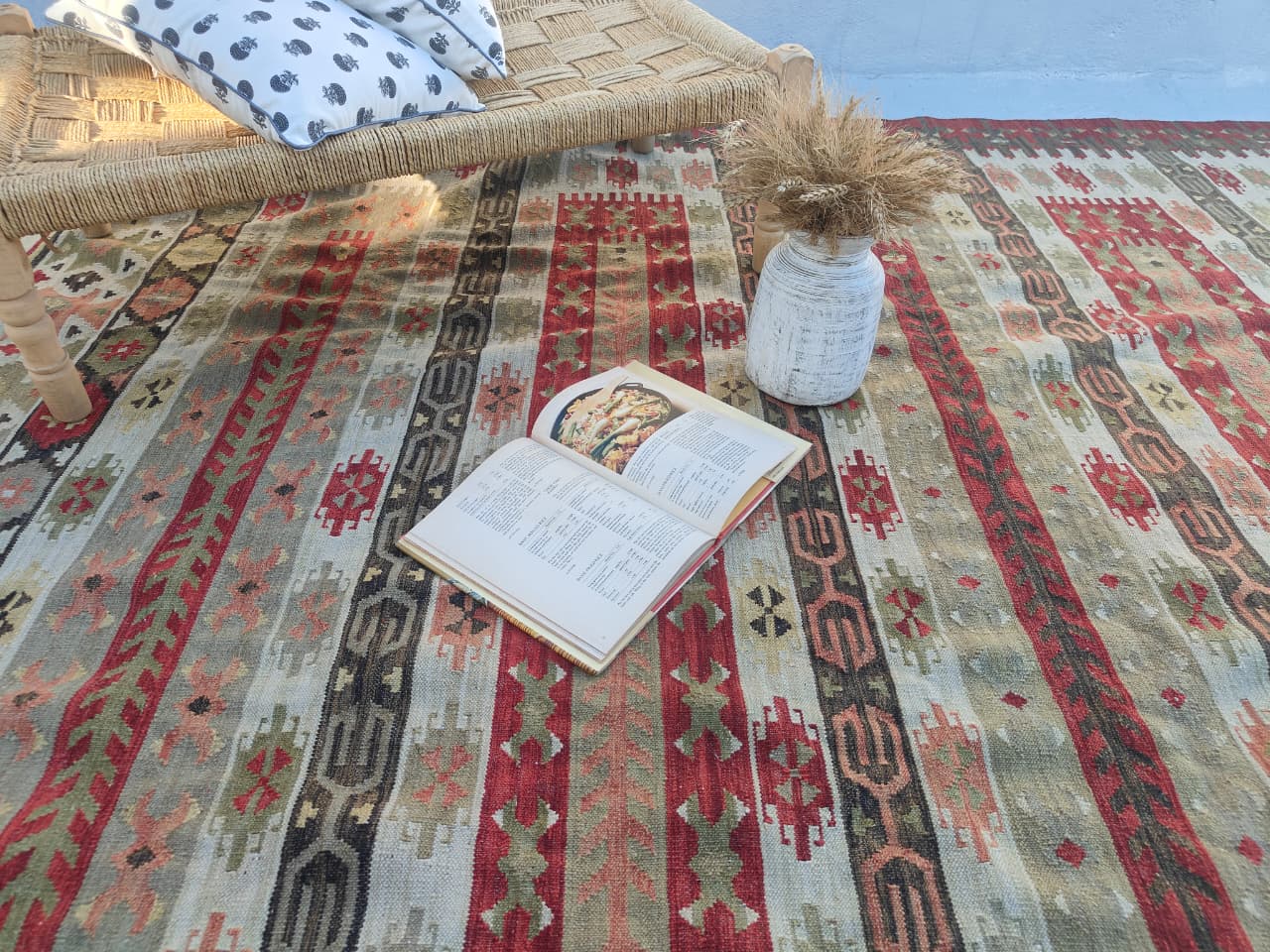Open book on a patterned rug with a vase and decorative item nearby