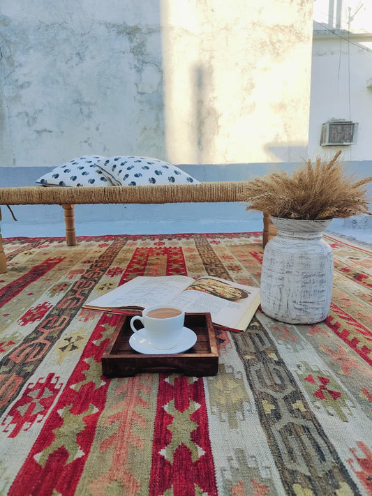 Café table with a cup of coffee, tray, and decorative items on a patterned rug.