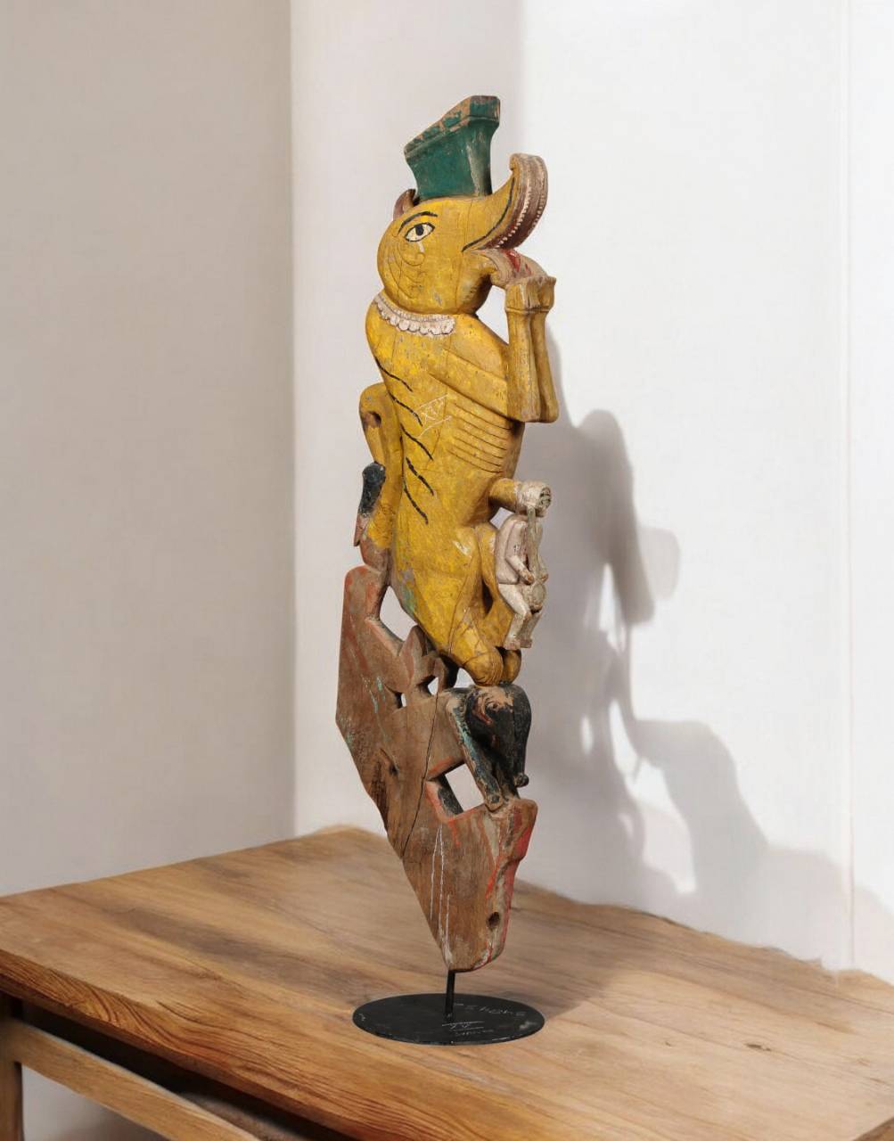 Wooden sculpture of a bird figure on a stand against a white wall