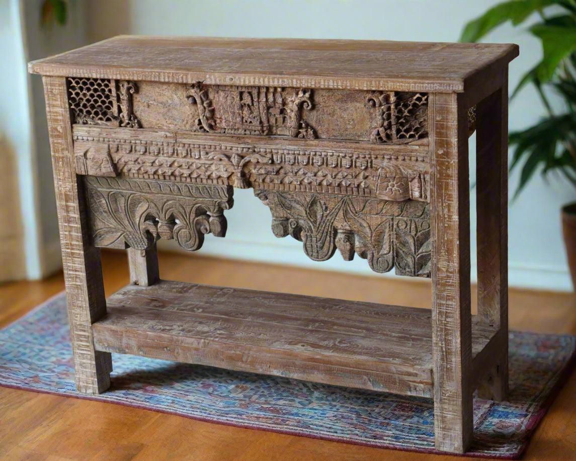 Carved wooden side table on a wooden floor with a plant in the background