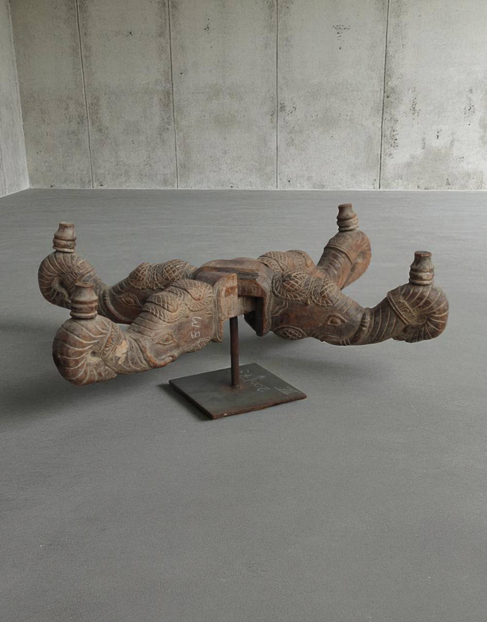 Decorative wooden sculpture on a stand in a minimalistic room with concrete walls and floor.