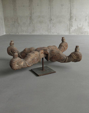 Decorative wooden sculpture on a stand in a minimalistic room with concrete walls and floor.