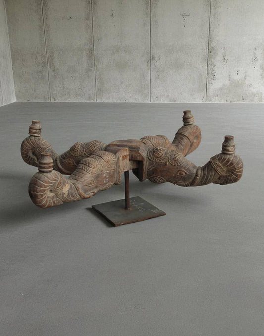Decorative wooden sculpture on a stand in a minimalistic room with concrete walls and floor.
