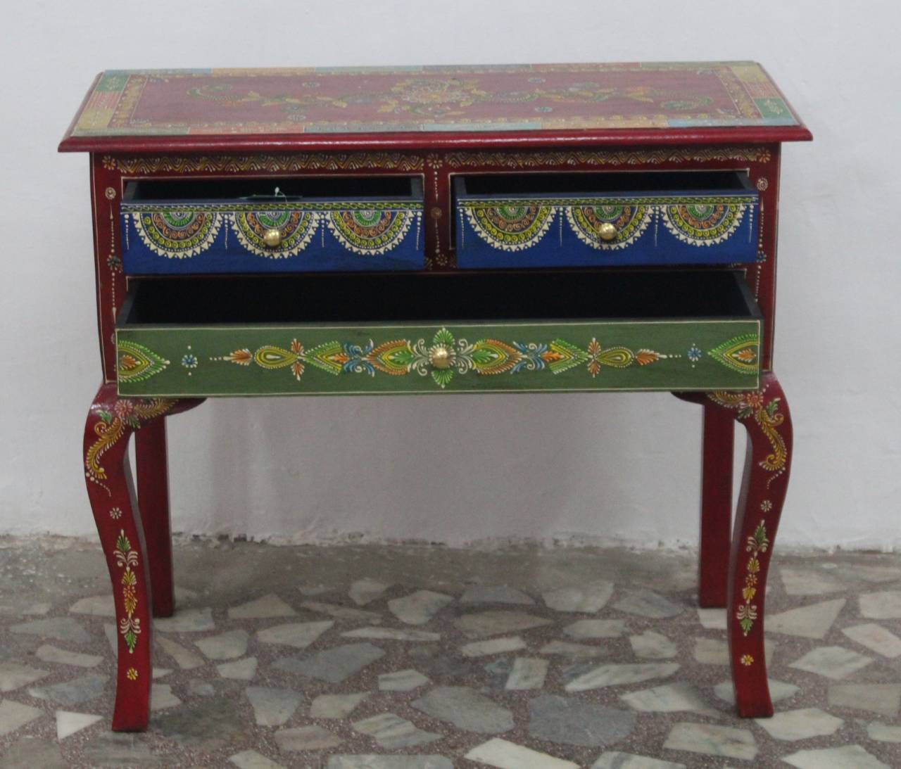 Colorful wooden side table with decorative patterns on a stone floor.