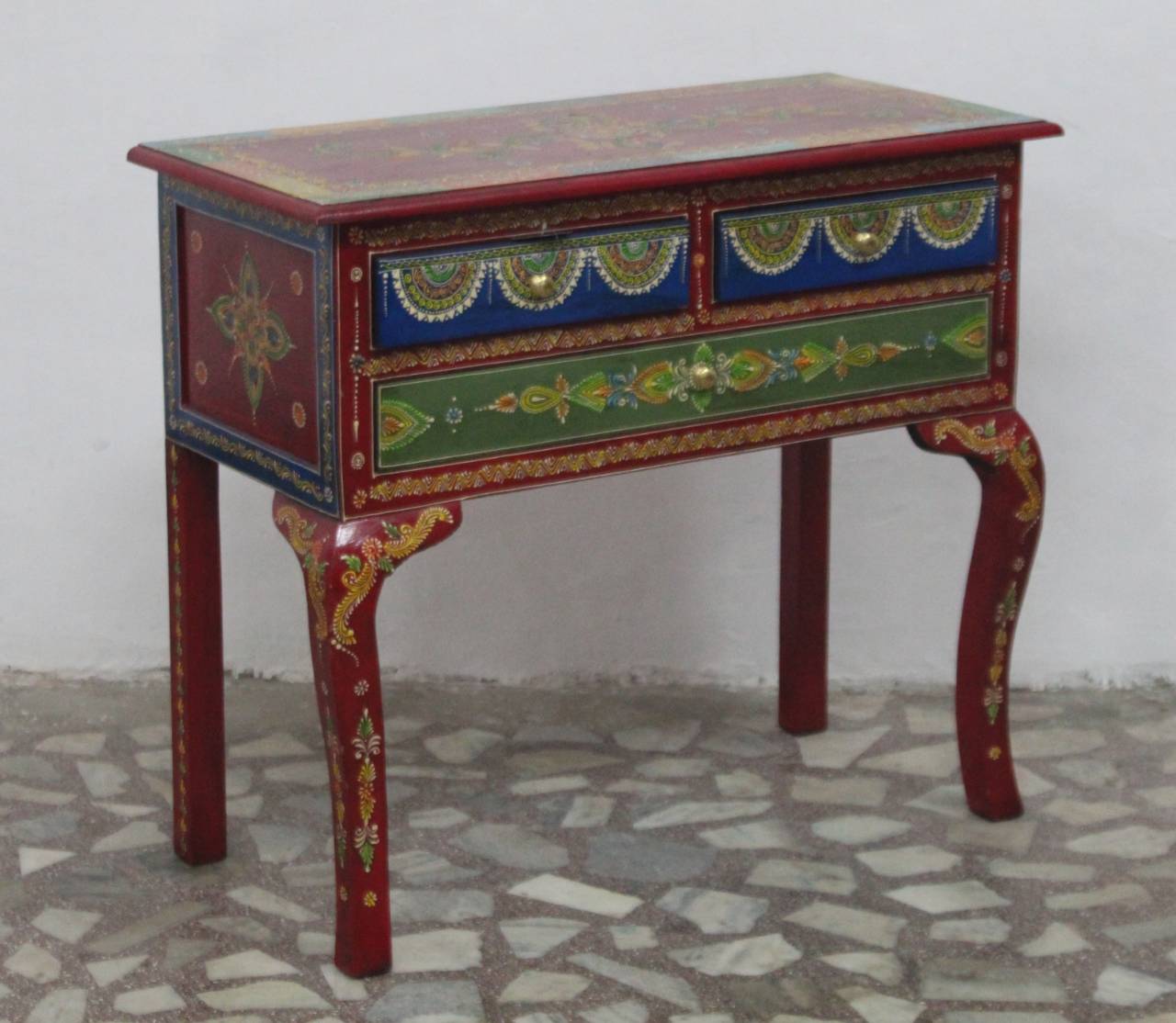 Decorative wooden table with colorful paintwork on a stone floor.