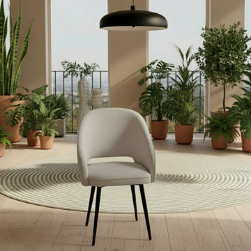 Gray chair with black legs in a room with plants and large windows.