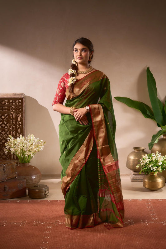 Woman in a green saree with a red blouse standing in a decorated room.