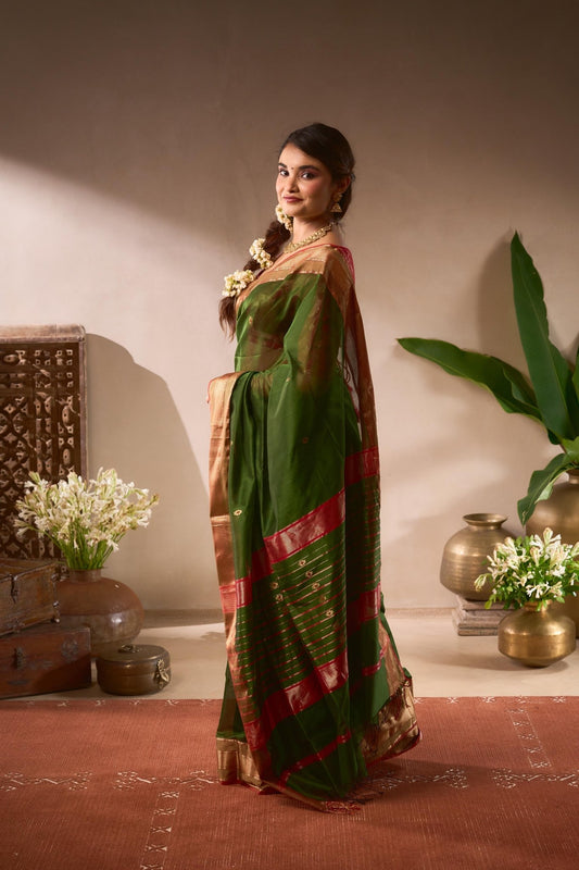Woman in a green and red saree standing in a room with decorative elements.