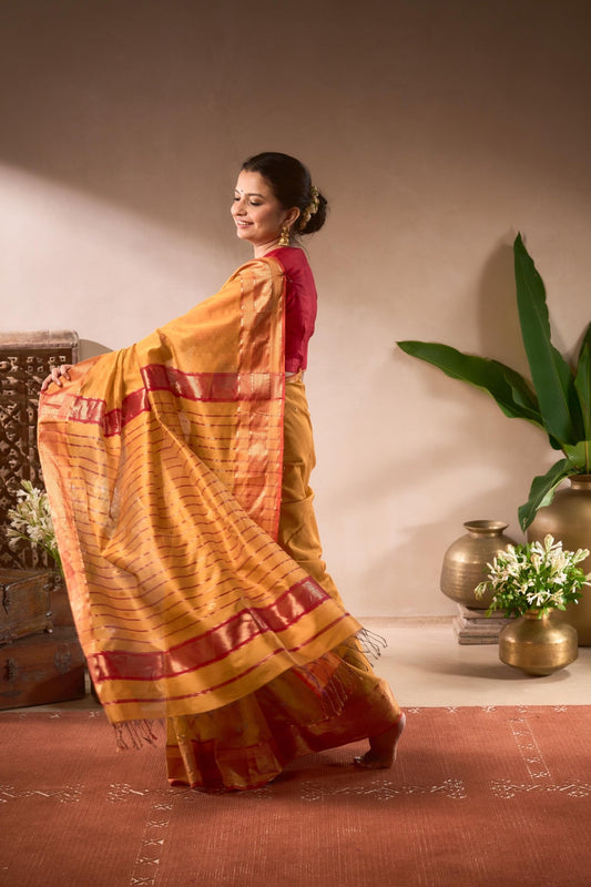 Woman in a yellow saree with red patterns standing in a room with decorative elements.