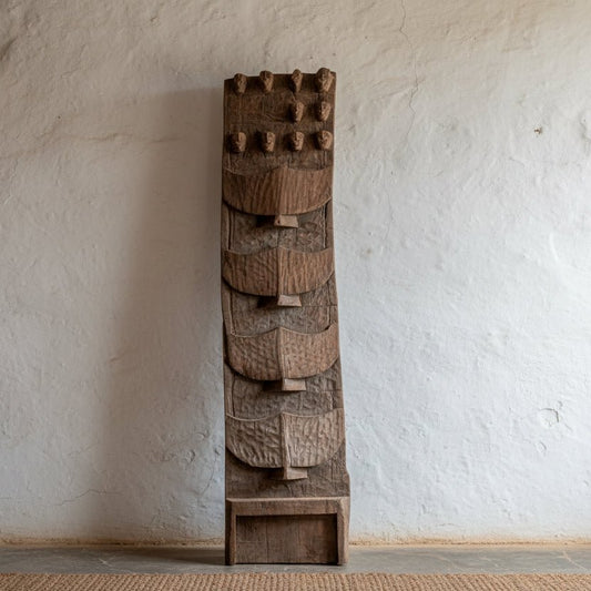Tall, textured wooden sculpture on a plain background