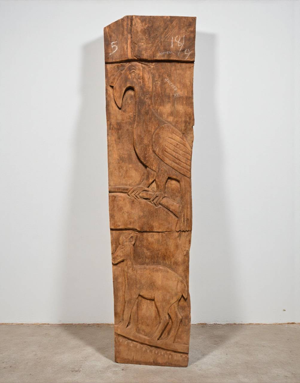Wooden panel with carvings of a bird and deer on a plain background