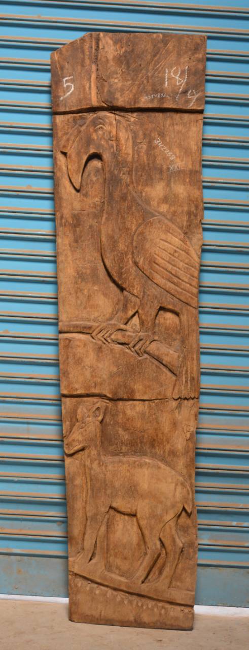 Wooden panel with carvings of a bird and a deer against a blue corrugated metal background.