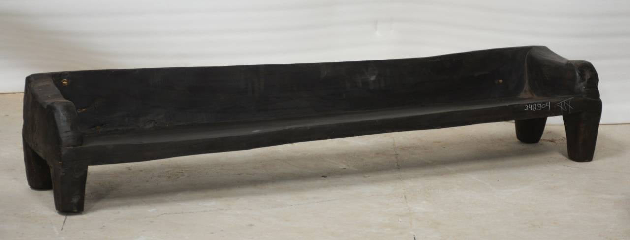 Long black stone bench on a light wooden floor with a white wall background