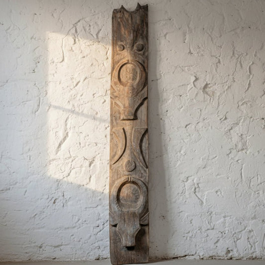 Tall wooden sculpture with carvings in a room with a table and decorative plants.