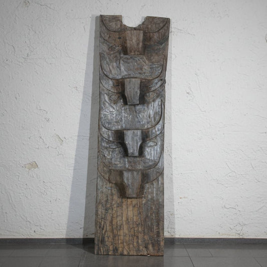 Wooden totem-like sculpture against a plain wall