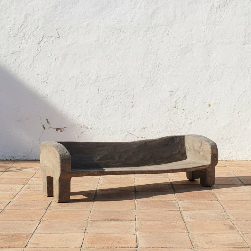 bench in front of a wooden table with plants and vases on a concrete floor.