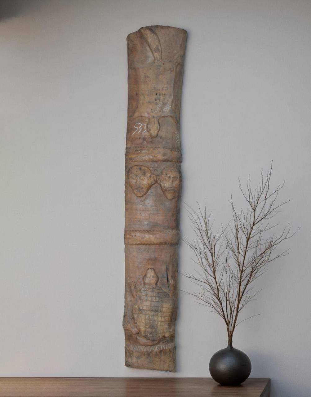Decorative stone column with carvings on a wooden shelf against a plain wall.