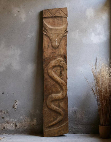 Wooden sculpture of a bull and snake against a textured wall.