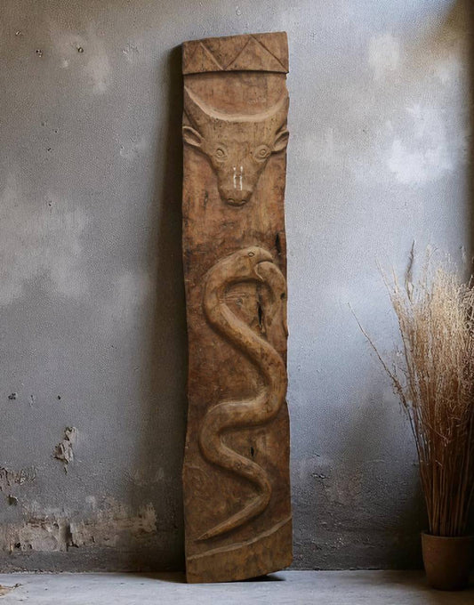 Wooden sculpture of a bull and snake against a textured wall.