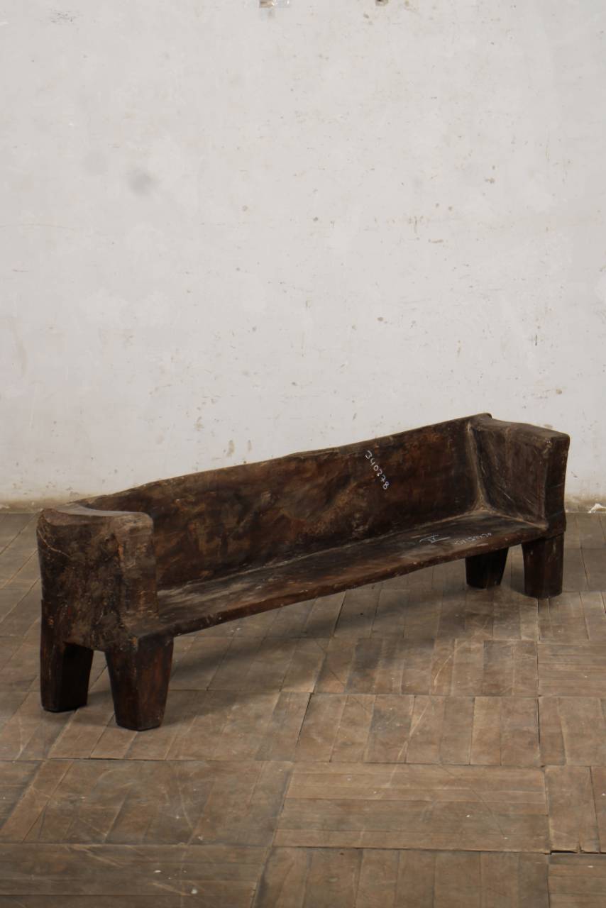 Wooden bench against a textured white wall on a tiled floor