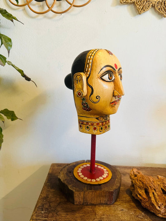Decorative head sculpture on a wooden base with a plain background