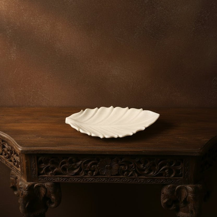 White ceramic leaf-shaped plate on a wooden table with a brown background