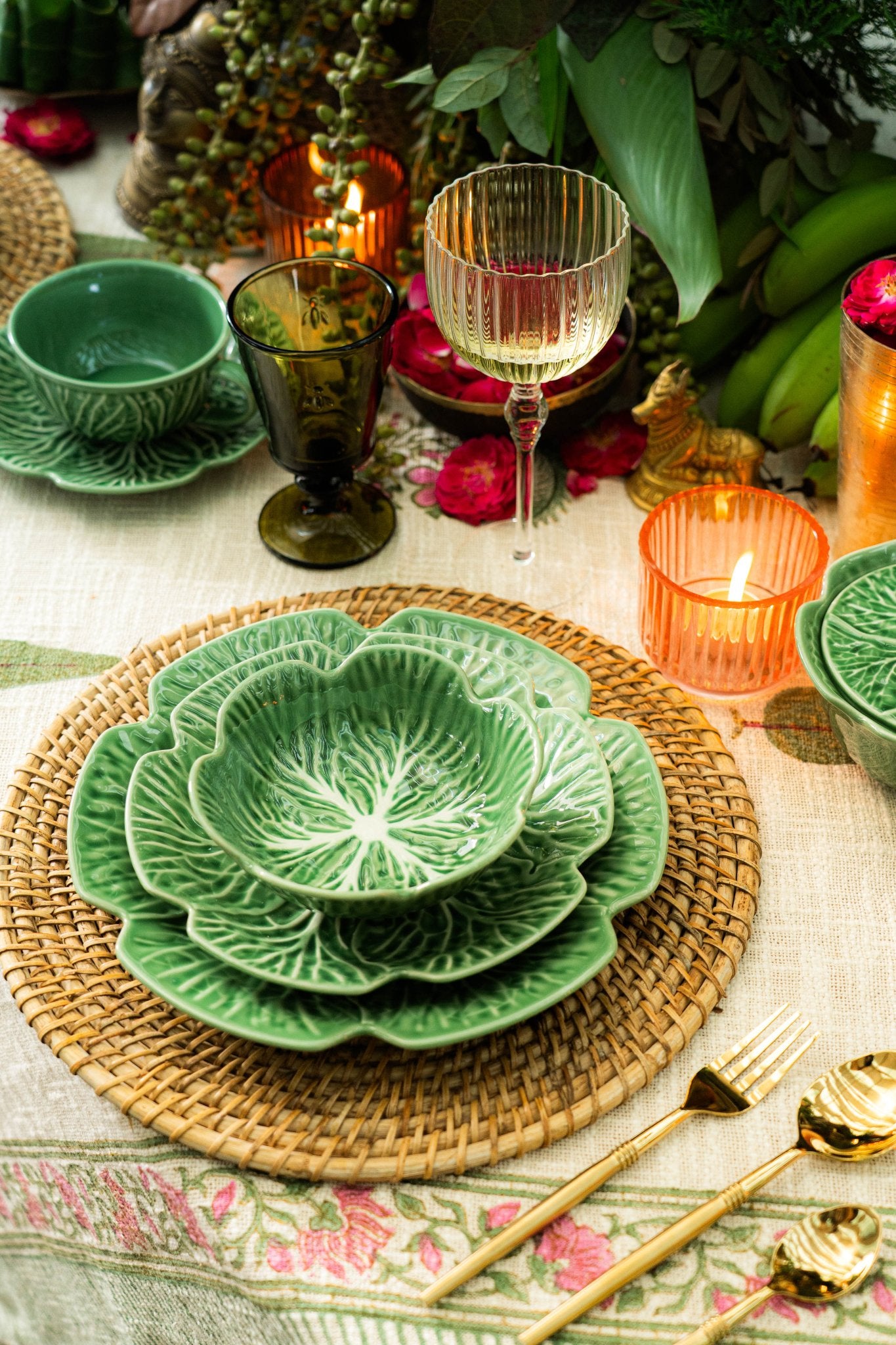 Decorative table setting with green leaf-patterned plates, gold cutlery, and candles.