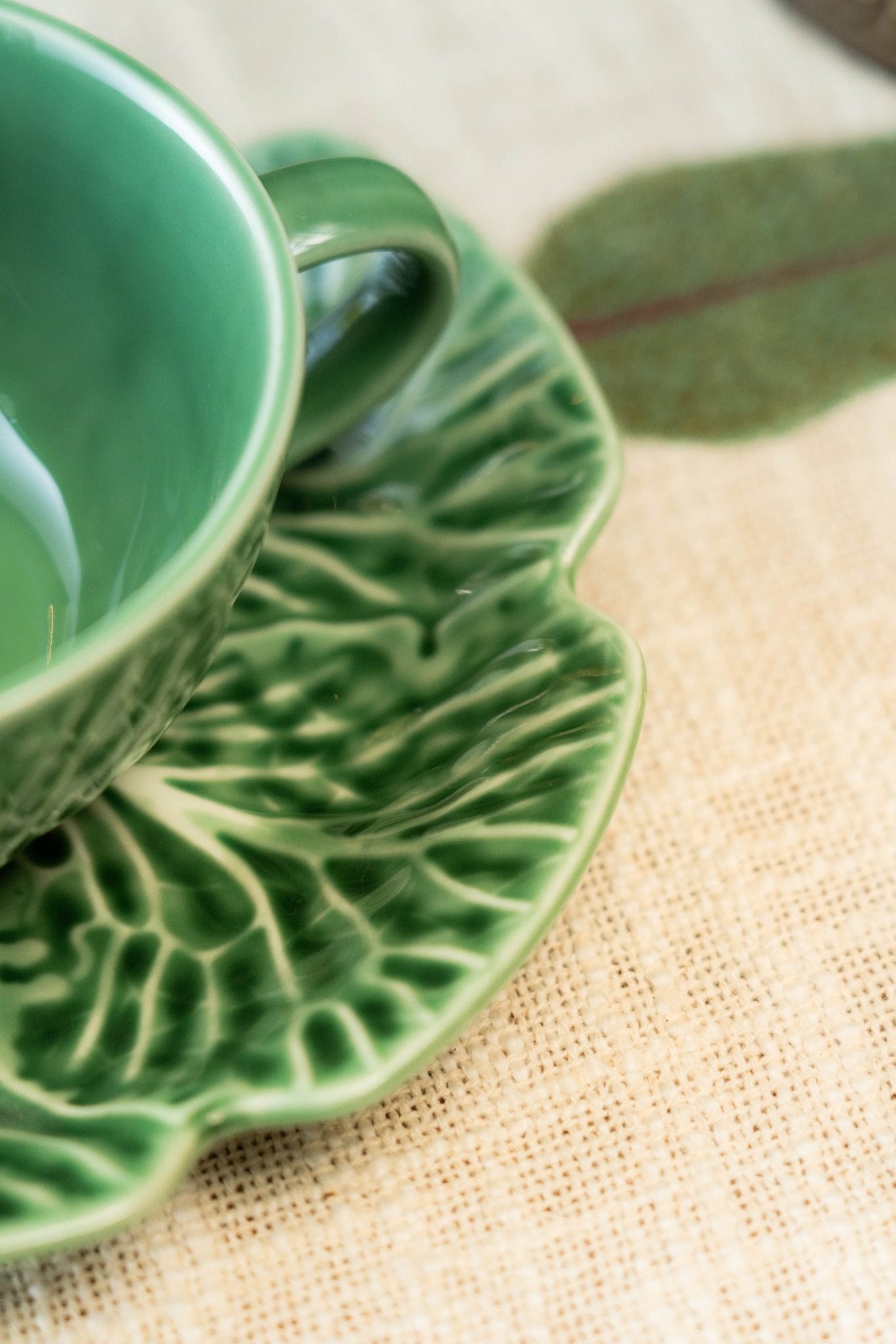 Green ceramic cup and saucer on a textured beige surface