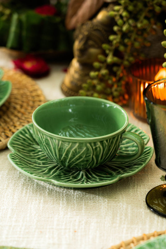 Green ceramic cup and saucer on a textured surface with decorative background