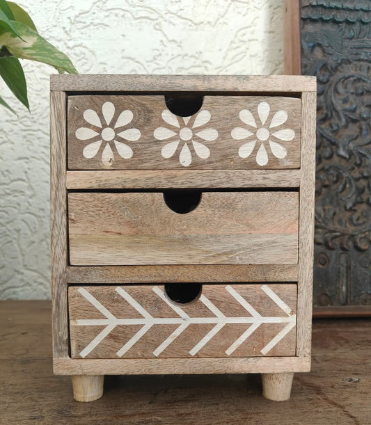 Wooden drawer unit with floral and arrow designs on a wooden surface.