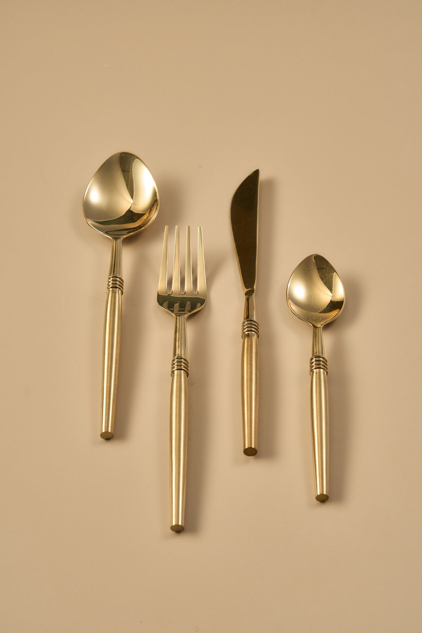 Set of gold-colored cutlery including a spoon, fork, and knife on a beige background