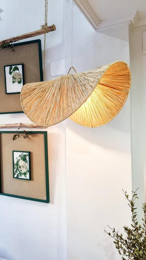 Woven lampshade hanging on a wall with framed pictures and a plant.
