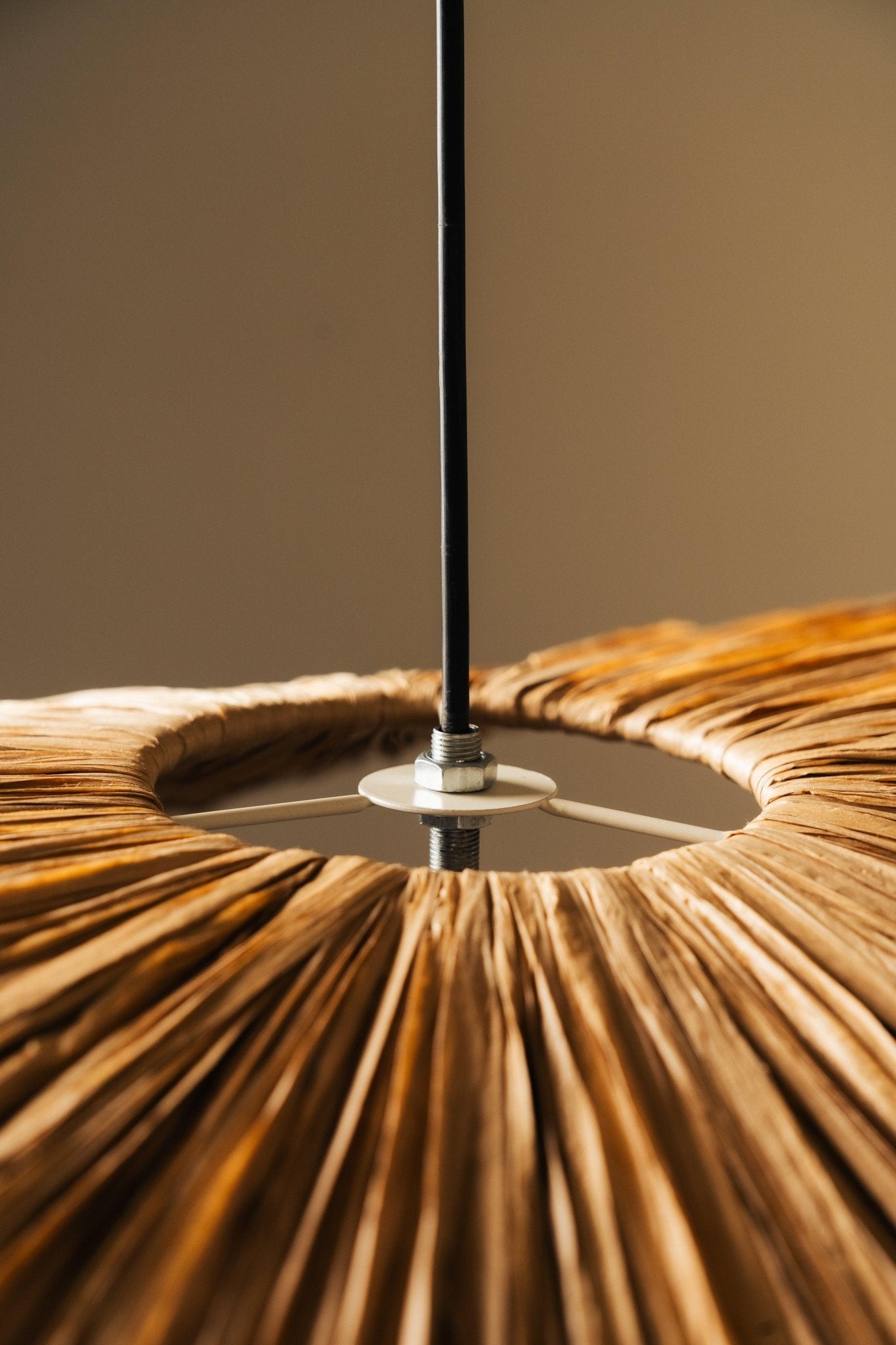 Close-up of a textured brown lampshade with a black rod against a neutral background