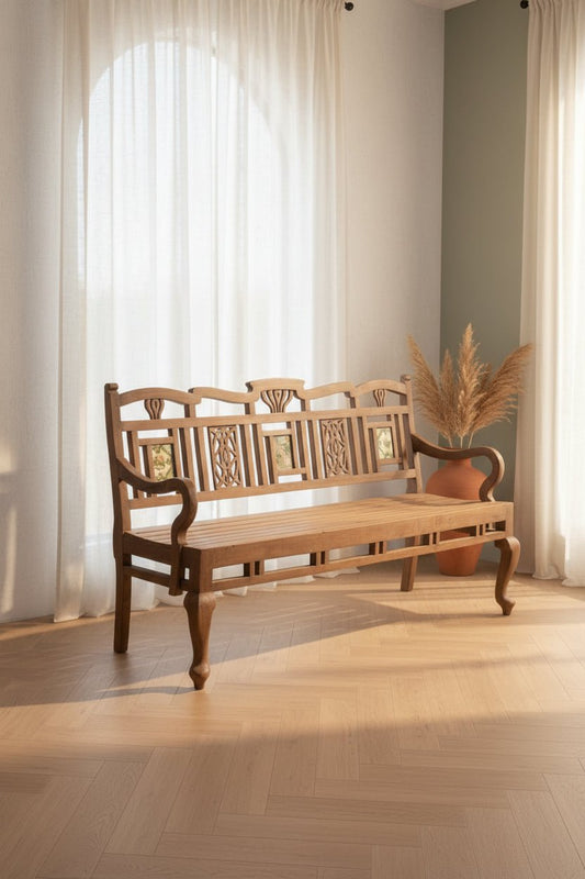 Wooden bench with decorative carvings in a room with light-colored curtains and wooden floor.