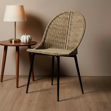 Wicker chair with black legs next to a wooden side table with a lamp and decorative items.