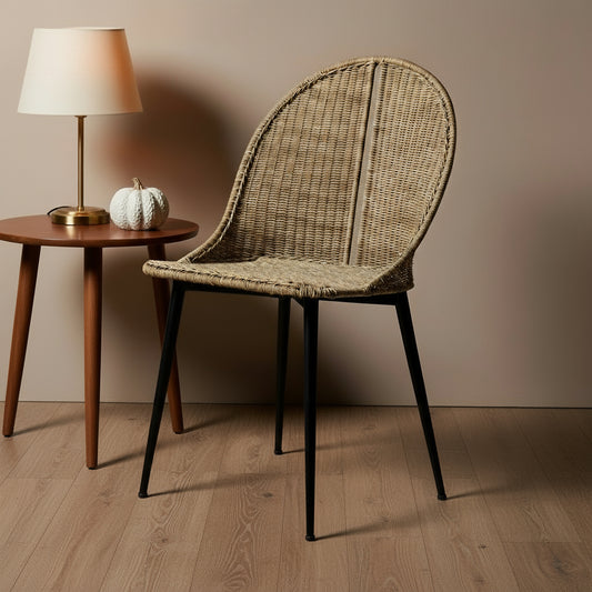 Wicker chair with black legs next to a wooden side table with a lamp and decorative items.