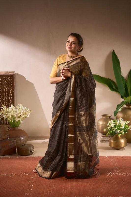 Woman in a traditional saree standing in a decorated room with plants and vases.